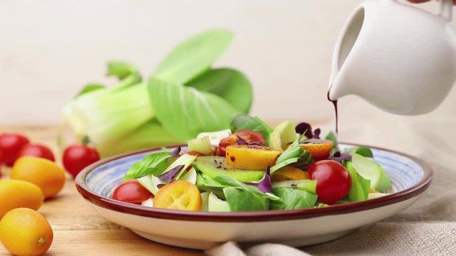 Vegetarian salad of pac choi cabbage, kiwi, tomatoes, kumquat, microgreen sprouts poured with vinegar. Side view, close up.