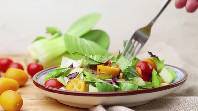 Vegetarian salad of pac choi cabbage, kiwi, tomatoes, kumquat, microgreen sprouts stir with a fork. Side view, close up.