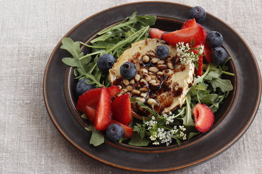 Baked goat cheese with honey, pine nuts, blueberries and strawberries on arugula pillow
