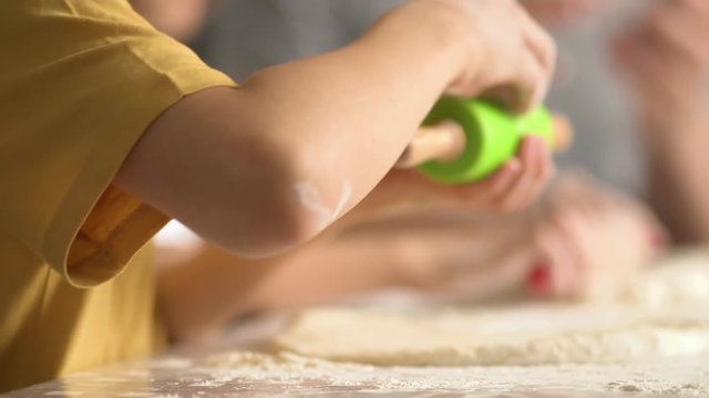 Children cooks pizza. Boy and girl having fun with father. Prepering ingredients for pizza. Roll out the dough with a rolling pin