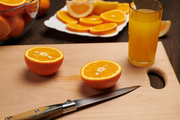 Fresh orange fruit whole and sliced on a wooden table, cutting board and kitchen knife. A plate full of citrus slices - natural and healthy food. Glass of fruit cocktail.