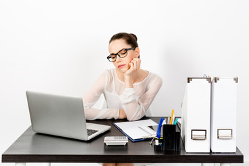 A young enerpreneur woman sits at her workplace with a laptop near a white wall while talking emotionally and loudly on the phone. The concept of successful business