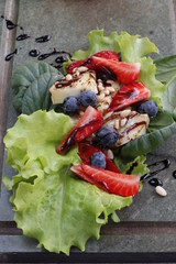 Baked goat cheese with honey, pine nuts, blueberries and strawberries on a fresh salad pillow