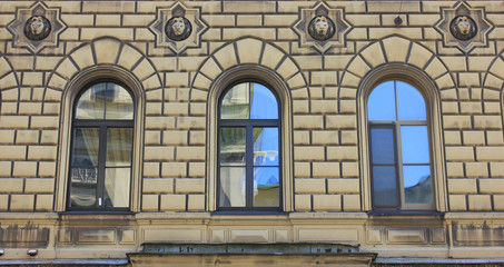 Three decorative windows on beige walls building facade in St Petersburg, Russia. Three simple arched windows, old exterior details of historic city house with light brown colored walls