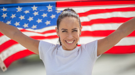 Smiling young attractive female holding American flag behind her back