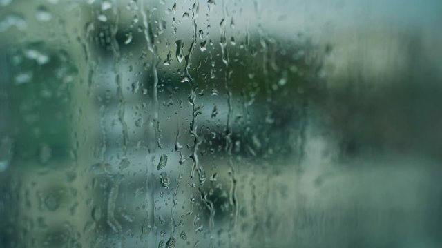 Falling drops on glass. Wet window on blur background. Rain drops running down the window surface.