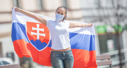 Slovak female fan holds a flag behind her on a street, wearing a face mask