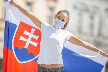 Smiling girl in a face mask holds a flag of Slovakia behind her on the street
