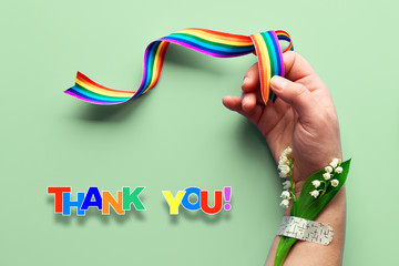 Rainbow ribbon in woman's hand. Chamomile flowers and grass bouquet attached to wrist with medical patch. Thank you doctors and nurses! Creative flat lay, top view on green mint background.