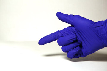 A hand in a blue rubber glove points to a place for the text. Index in the concept of medicine, hand protection, sterility. White background, isolate