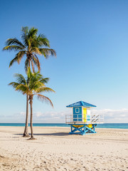 Colorful blue and yellow lifeguard station on beach with palm trees and blue sky copy space.