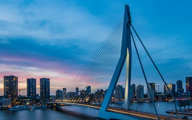 Foto op Plexiglas Erasmusbrug Lange sluitertijd geschoten op de Erasmusbrug in Rotterdam, Nederland, tijdens het blauwe uur met uitzicht over de prachtige wolkenkrabbers.