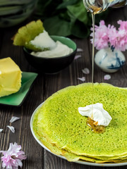 Spinach pancakes with sour cream, maple sorop pouring on green pancakes, wooden dark background. Close-up, breakfast