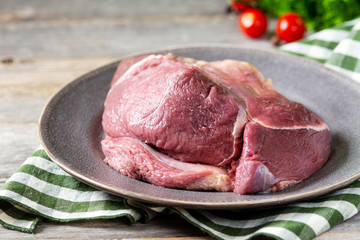 Raw beef ham in a ceramic plate on a light gray wooden table. Beef meat