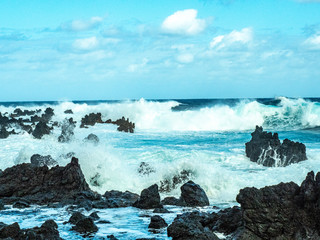 Big waves crash close to shore with aquamarine seas, white foam, sand and blue skies.