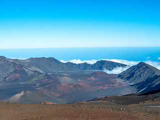 Crater walls of Maui's Haleakala Volcano with fluffy white clouds below and blue sky copy space above.