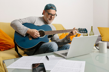 Musician playing the guitar and composing music with his colleagues by video conference through his...