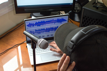 Person with cap and headphones recording a podcast at home using microphone and computers....