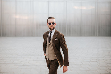 Fashion business wear model in brown suit and tie. Outdoor photoshoot in white wall background concept for magazine cover and man’s brochure clothing images.