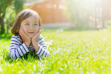 cheerful little boy with a dreamy look lies on the lawn on a sunny summer day