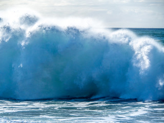 Fototapeta na wymiar Big waves crash close to shore with aquamarine seas, white foam, sand and blue skies.