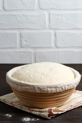 Freshly cooked yeast dough in a basket for baking of fresh natural cakes and cookies on a dark wooden background.
