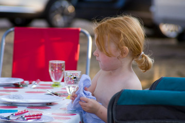 Kleines rothaariges Mädchen deckt beim Campingurlaub den Tisch