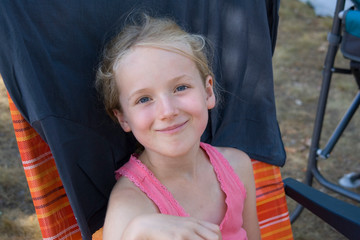 Lächelndes blondes Mädchen im rosa Top sitzt in einem Liegestuhl im Sommerurlaub beim Camping