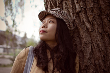 Attractive Asian Female College Student Looking Into The Distance While Leaning Against A Tree