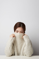Studio shot of happy asian woman wears beige knitted jumper, holds hands under chin. Vertical shot. Isolated.