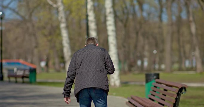 Man became ill on the street, severe shortness of breath. Man sits down on a bench and coughs heavily. Symptoms of coronavirus, covid virus. Man got coronavirus. View from the back.