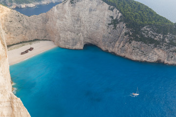 Idyllic view of the beautiful Navagio beach with a sailboat sailing nearby on the island of Zakynthos in Greece.