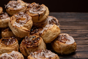 Homemade glazed puff pastry cinnamon rolls with custard and raisins on wooden background.