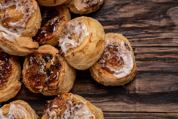 Homemade glazed puff pastry cinnamon rolls with custard and raisins on wooden background.