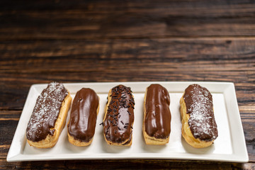 Profiteroles with cream and chocolate. Eclairs with black chocolate on wooden background. Traditional French dessert. Selective focus.