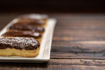 Fototapeta na wymiar Profiteroles with cream and chocolate. Eclairs with black chocolate on wooden background. Traditional French dessert. Selective focus.