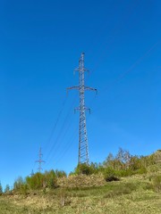 Obraz premium High voltage power stations standing in a field among green grass on a hill