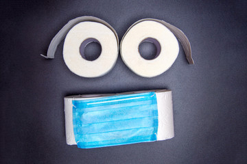 toilet paper rolls are laid out in the form of an emoticon with a blue medical face mask. on a black background. virus outbreak concept. coronavirus news