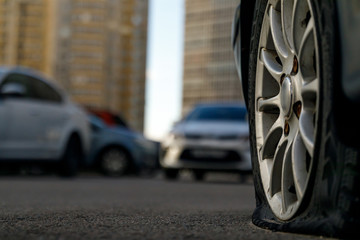 Car tire with a flat tire in the yard near a multi-storey building. Image of an accident, damage, breakdown for illustration on the topic of repair, insurance. Selective focus.
