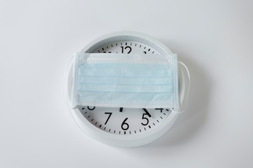White wall clock and medical mask over for protection COVID-19 coronavirus.