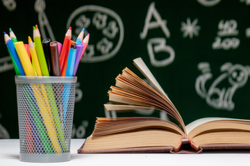 Back to school background with books, pencils and globe on white table on a green blackboard background.