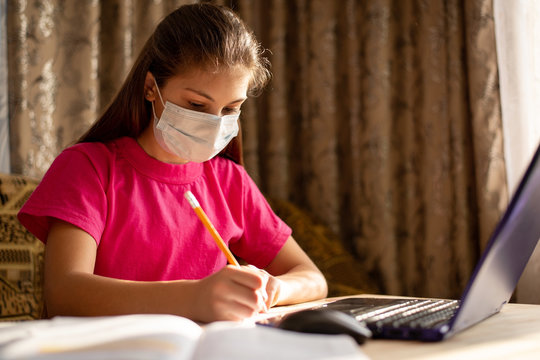 Girl in medical mask and pink t-shirt studying online. Concept of distance learning during global pandemic