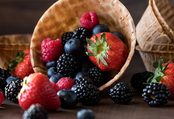 A macro close up view of a variety of berries spilling out of a waffle bowl. Delicious dessert ingredients concept.