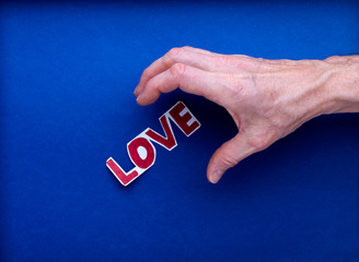 Une main d'homme va saisir un texte imprimé love, amour en rouge, sur fond bleu