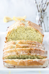 A close up front facing view of a lemon poppy seed loaf sliced into and a small vase of pussy willows in behind.