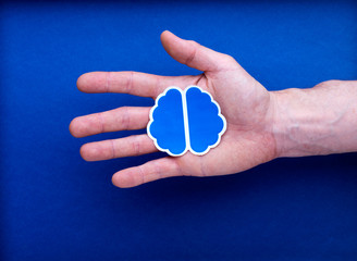 Illustration cerveau tenue par main homme sur fond studio bleu : imaginer, création, créatif,...