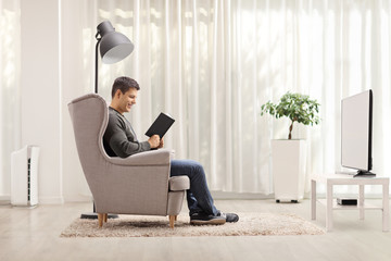 Profile shot of a man reading a book and sitting in an armchair