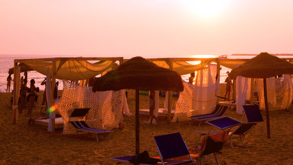Gazebos and straw umbrellas on the beach at sunset