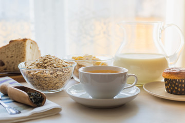 Fototapeta na wymiar Healthy simple food concept, breakfast - cup of tea, oatmeal with banana chips, fresh muffin and bread and a jug of milk