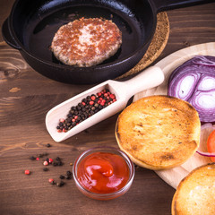 Cooking a delicious homemade burger, ingredients - fried bun, cutlet, lettuce, tomato, onion and sauce